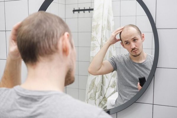 problème de perte de cheveux un homme regardant d'un œil critique le miroir dans la salle de bain tenant une tondeuse à cheveux. traitement pour l'alopécie androgénétique