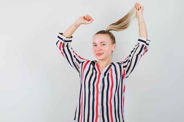 jeune femme posant avec des cheveux volants dans une chemise rayée et ayant l'air charmante