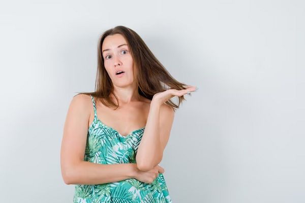 jeune femme tenant une mèche de cheveux dans son chemisier et ayant l'air perplexe vue de face. Cheveux à faible volume