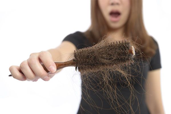 Femme montrant une brosse à cheveux pleine de cheveux