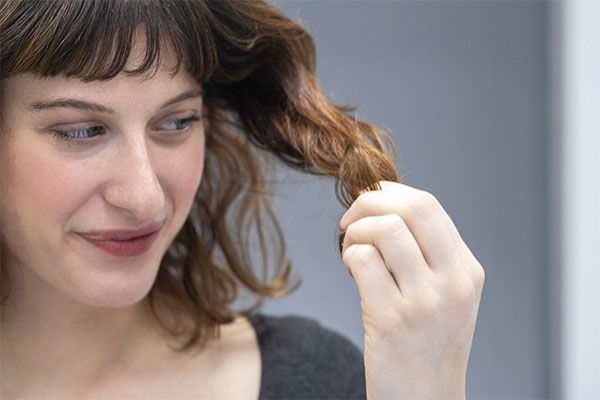 Belle femme regardant ses cheveux et les tenant avec sa main, Pourquoi les jeunes femmes perdent-elles leurs cheveux ?