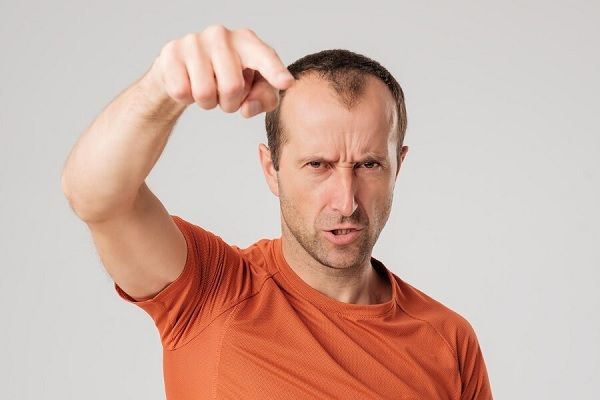 Homme mûr en t-shirt orange doigt pointant vers la caméra sur fond gris