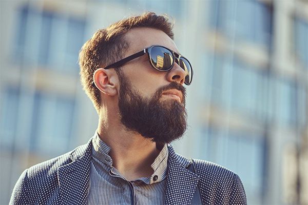 Portrait en gros plan d'un homme barbu portant des vêtements décontractés et des lunettes de soleil, debout dans une rue de la ville contre un gratte-ciel. le Minoxidil 5