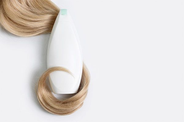 Bouteille de shampoing ou d'après-shampoing enveloppée dans une mèche de cheveux blonds bouclés, isolée sur fond clair. les meilleurs shampooings pour stimuler la croissance des cheveux