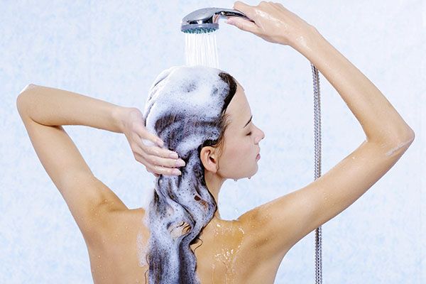 Femme se lavant les cheveux sous un jet d'eau, isolée sur fond blanc.