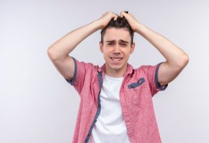 Un jeune homme caucasien inquiet, vêtu d'une chemise rose, se tient la tête à deux mains sur le mur blanc isolé.