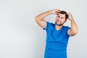 Jeune homme portant ses doigts à la tête, vêtu d'un T-shirt bleu et l'air irrité.