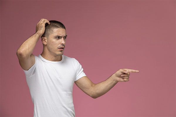 Vue de face d'un jeune homme en chemise blanche posant avec une expression confuse sur un fond rose. santé mentale impact cheveux