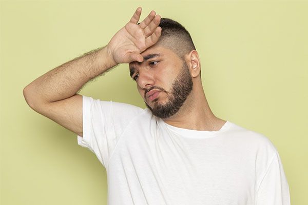 Un jeune homme caucasien malade passe la main sur le front.