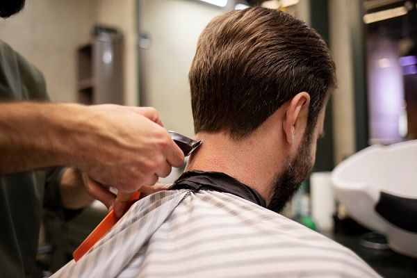 Homme barbu se faisant couper les cheveux au salon de coiffure. coupes de cheveux idéale pour les visages ronds