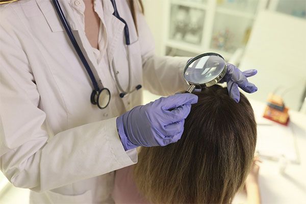 Un médecin spécialiste examine le cuir chevelu d'une femme à l'aide d'une loupe.