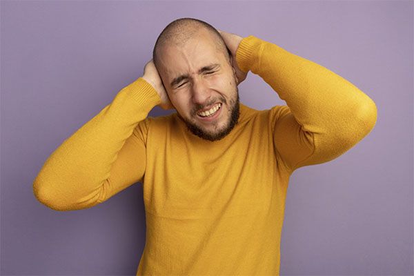 Homme en pull jaune au visage inquiet se bouchant les oreilles.