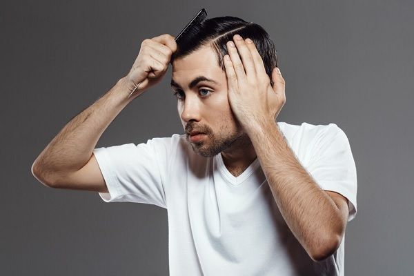 Homme en chemise blanche se peignant le cuir chevelu avec une brosse à cheveux. 
