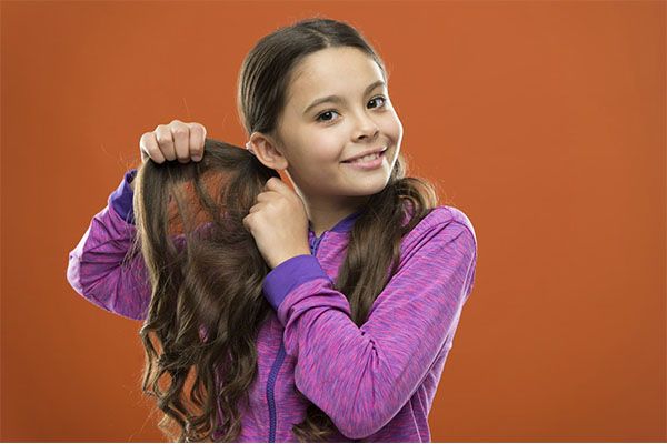 Une belle jeune fille en pull violet tresse ses cheveux avec ses mains.