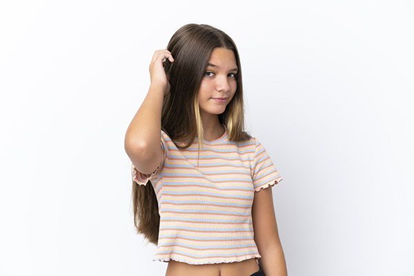 Fille aux cheveux bruns et à la chemise rose rayée, la main sur la tête.