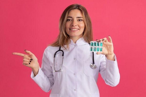 Jeune femme médecin souriante portant une blouse médicale avec un stéthoscope tenant des pilules