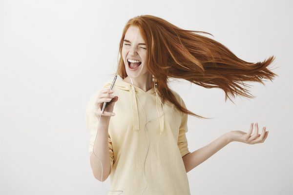 Jeune fille rousse heureuse jouant au karaoké sur son smartphone et chantant dans ses écouteurs.