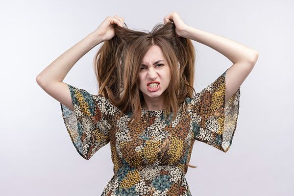 Femme stressée en robe colorée se tirant les cheveux. Le syndrome des ovaires polykystiques et la perte de cheveux sont-ils liés ?