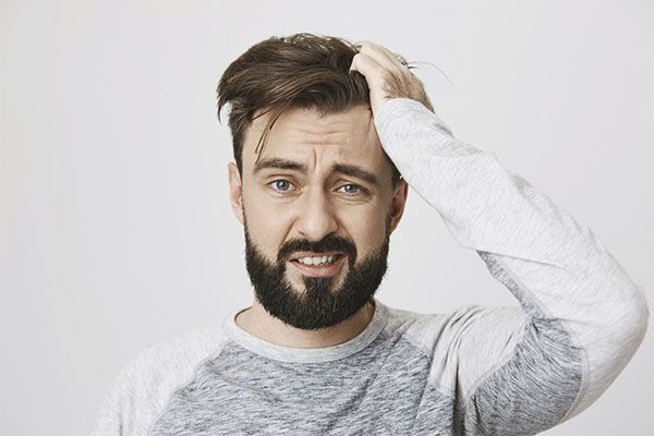 Homme en pull gris, visage inquiet et main sur la tête. Qu'est-ce que l'« effet shedding » ?
