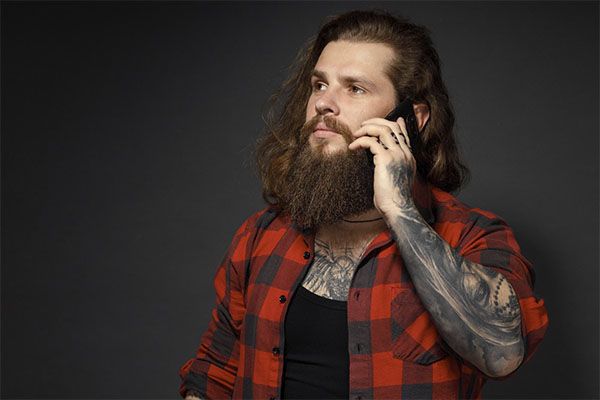 Homme tatoué aux cheveux longs et à la chemise à carreaux rouges parlant au téléphone.