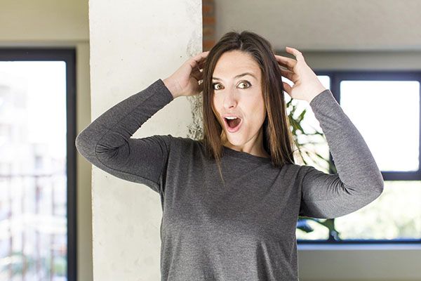 Femme aux cheveux bruns, la main sur la tête, l'air surpris. L'alopécie ménopausique