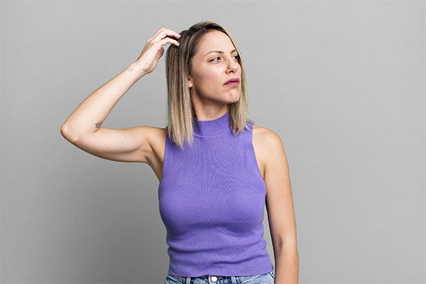 Femme aux cheveux bruns, la main sur la tête, regardant sur le côté. 
