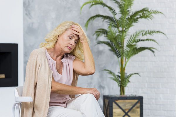 Femme blonde, la main sur la tête, assise sur une chaise. 