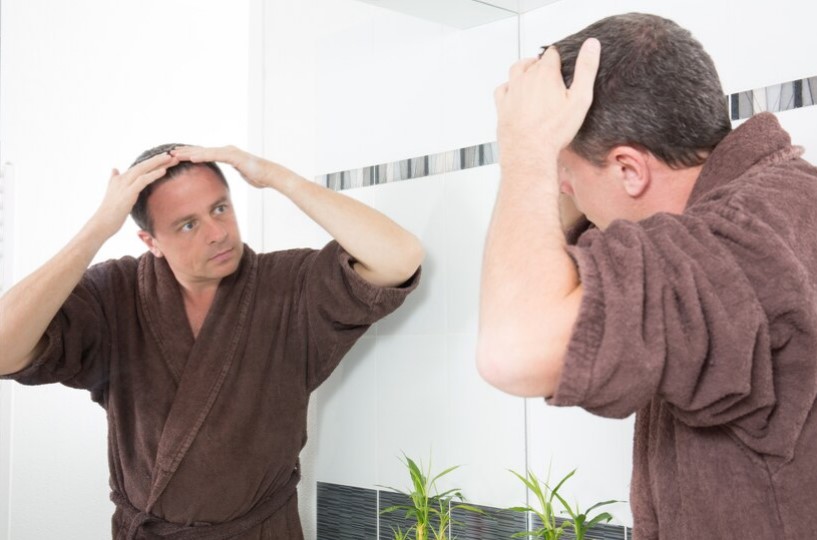 Un homme contrôle la perte de ses cheveux dans la salle de bain en se regardant dans un miroir et en se coiffant.