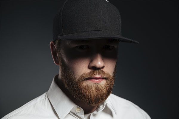 Homme blond en chemise blanche avec une casquette noire. Le port d'un chapeau fait-il tomber les cheveux