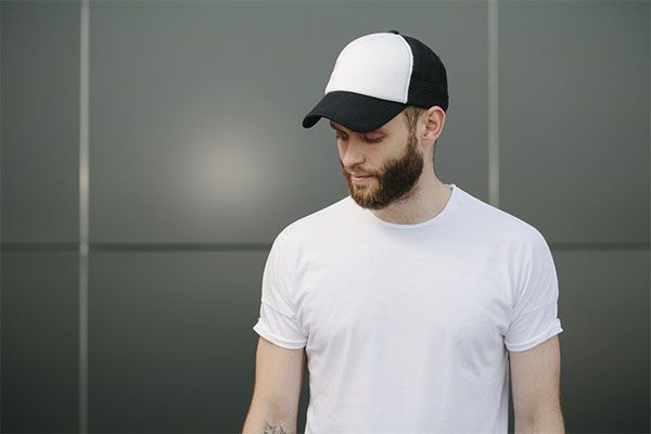 Homme en chemise blanche avec une casquette noire et blanche posant.