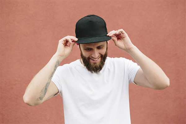 Homme en chemise blanche et casquette noire posant. Le port d'un chapeau fait-il tomber les cheveux