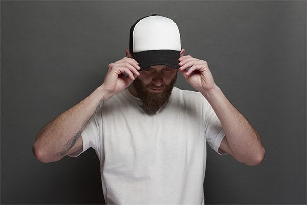 Homme en chemise blanche avec une casquette noire et blanche posant.