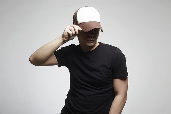 Homme en chemise noire avec une casquette noire et blanche posant.
