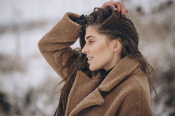 femme aux cheveux noirs avec un gilet marron pour le froid, les mains sur la tête. 