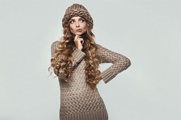Femme aux cheveux bruns portant une robe tissée et un bonnet brun. prendre soin de vos cheveux pendant l'hiver
