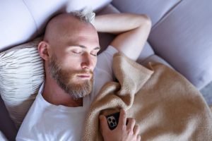 Un jeune homme s'endort sur le canapé avec son téléphone portable