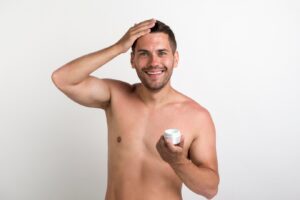Jeune femme souriante tenant un récipient de crème capillaire et regardant l'appareil photo.