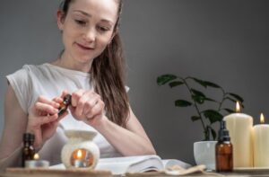 Un livre est posé sur la table, des bougies brûlent et une femme verse de l'huile essentielle dans une lampe aromatique. Concept de lecture dans une atmosphère relaxante, style de vie aromathérapie, rituels du soir et du matin. La dermatite séborrhéique
