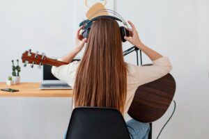 Vue arrière d'une musicienne mettant un casque pour enregistrer une chanson et jouant de la guitare acoustique.