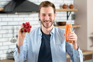 Portrait d'un jeune homme tenant un navet rouge et une carotte orange. vitamines pour prévenir l'alopécie