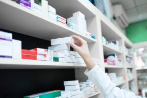 Vue rapprochée de la main d'un pharmacien prenant une boîte de médicaments sur une étagère dans une pharmacie.