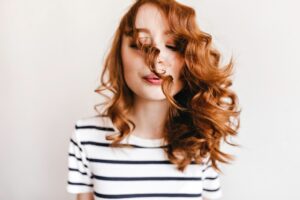 Charmante femme rousse soufflant sur ses cheveux bouclés. Femme caucasienne enjouée.