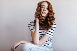 Femme rousse intéressée par les jeans, assise et regardant. Photo d'intérieur d'une jeune fille rousse de bonne humeur dans un T-shirt décontracté à la mode.