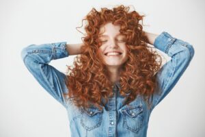 Portrait touchant d'une belle fille rusée souriant les yeux fermés sur fond blanc.