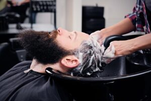 Image en gros plan d'un coiffeur lavant les cheveux d'hommes barbus avant qu'ils ne se fassent couper les cheveux dans un salon de coiffure.