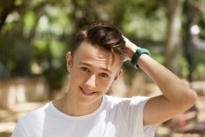 Jeune garçon, vêtu d'un T-shirt blanc, dans un parking - prendre soin de ses cheveux en ete