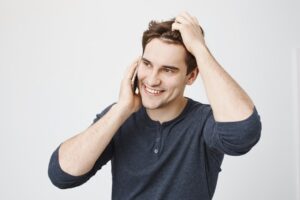 Bel homme souriant parlant au téléphone et se passant la main dans les cheveux