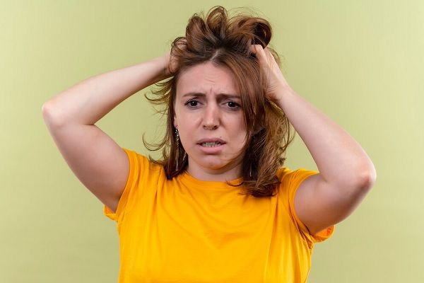 Jeune femme décontractée anxieuse tenant ses cheveux dans un espace vert isolé. Quelle est l’ampleur normale de la perte de cheveux chez les femmes 