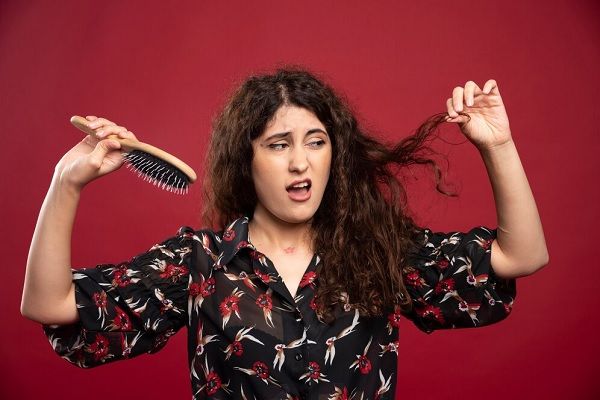 Femme bouclée tenant un peigne. Quelle est l’ampleur normale de la perte de cheveux chez les femmes 
