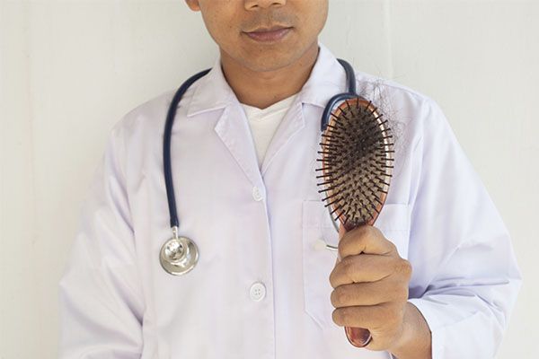 Un homme vêtu d'une blouse blanche, tenant une brosse sur laquelle se trouvent des résidus de cheveux. chirurgien de greffe de cheveux